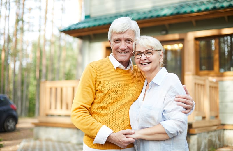 Senior couple smiling outside their home
